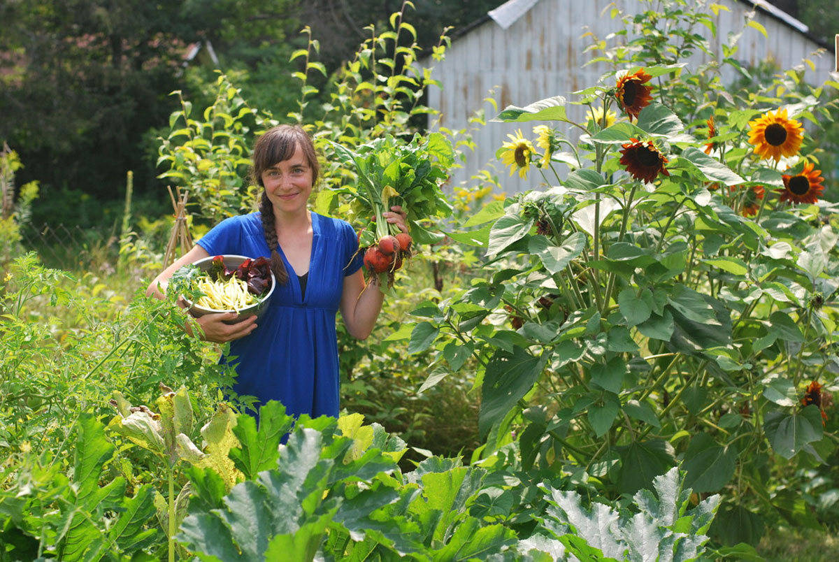 Une femme debout dans son potager, des légumes à la main